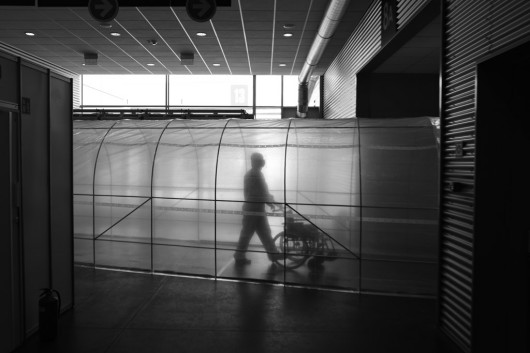 Kategoria: Zdjęcia pojedyncze - wydarzenia. III nagroda. Autor: Przemysław Błaszkiewicz, „Magazyn Pielęgniarki i Położnej”
Hermetyczny tunel łączący oddziały strefy skażonej szpitala tymczasowego na terenie poznańskich targów przebiega eksterytorialnie przez korytarz strefy czystej. Na zdjęciu odziany w kombinezon ochronny medyk przemieszcza się z wózkiem inwalidzkim między oddziałami.