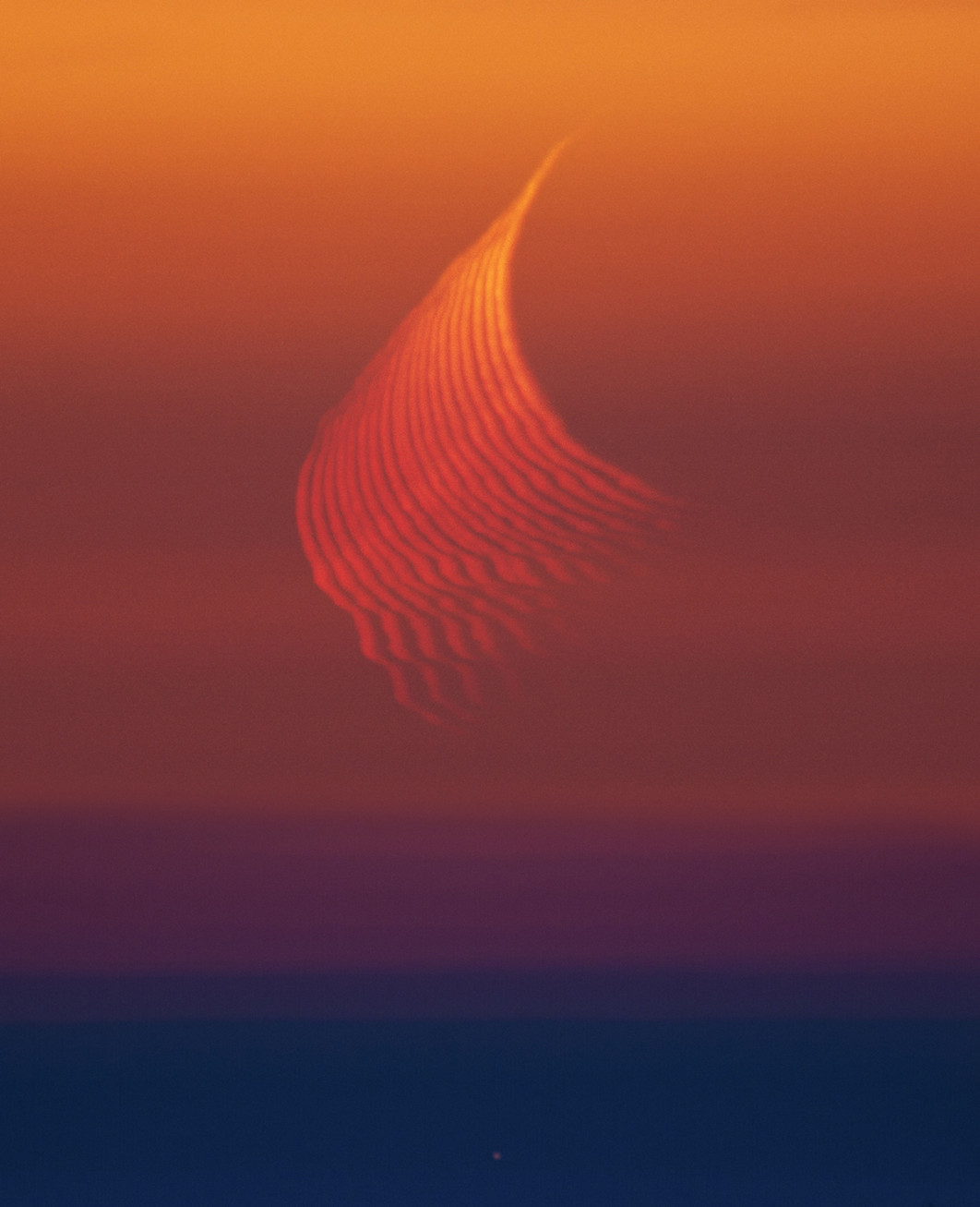 Fot. Marcella Giulia Pace, "The Trace of Refraction", 1. miejsce w kat. Our Moon / ZWO Astronomy Photographer of the Year 2025

Zdjęcie ukazuje zjawisko refrakcji atmosferycznej: światło Księżyca, przechodząc przez gęste warstwy atmosfery blisko horyzontu, załamuje się w sposób podobny do promieni światła w pryzmacie. Czerwony odcień Księżyca powodowany jest przez tzw. rozpraszanie Rayleigha (mniejsze cząsteczki w atmosferze silniej rozpraszają krótsze długości fal, przez co przeważają dłuższe fale - czyli czerwień).