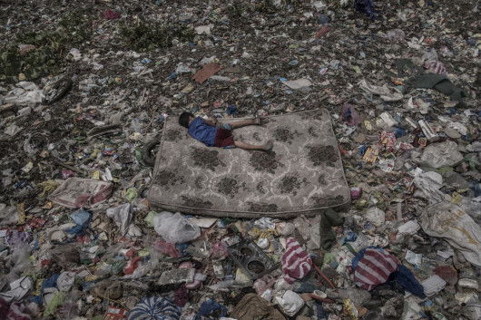 fot. Mario Cruz, Living Among What's Left Behind, 3. miejsce w kategorii Environment.

Dziecko na materacu zbiera produkty nadające się do przetworzenia ze śmieci unoszących się na rzece Pasig na Filipinach. Rzeka ta została ogłoszona biologicznie martwą już w latach 90. XX wieku, w skutek zanieczyszczenia przemysłowego i wypuszczania nieoczyszczonych ścieków przez zamieszkujące jej wybrzeża społeczności. Zaliczana jest do 20 najbardziej zanieczyszczonych rzek na świecie. Co roku z jej nurtem do oceanu wpada 64 tys. ton plastiku. Podejmowane są działania mające za zadanie jej oczyszczenie, ale nadal na niektórych odcinkach zanieczyszczenie jest tak ogromne, że możliwe jest chodzenie po unoszących się na niej odpadach.