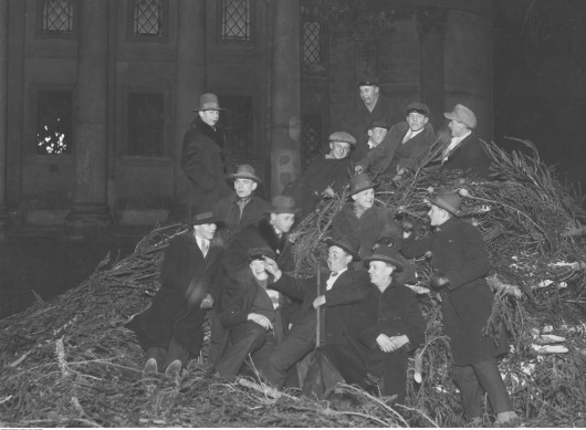 Grupa młodych mężczyzn na stosie niesprzedanych choinek, w oczekiwaniu na rozpoczęcie pasterki. W tle widoczny kościół św. Aleksandra, Warszawa, 1926 / 
Narodowe Archiwum Cyfrowe