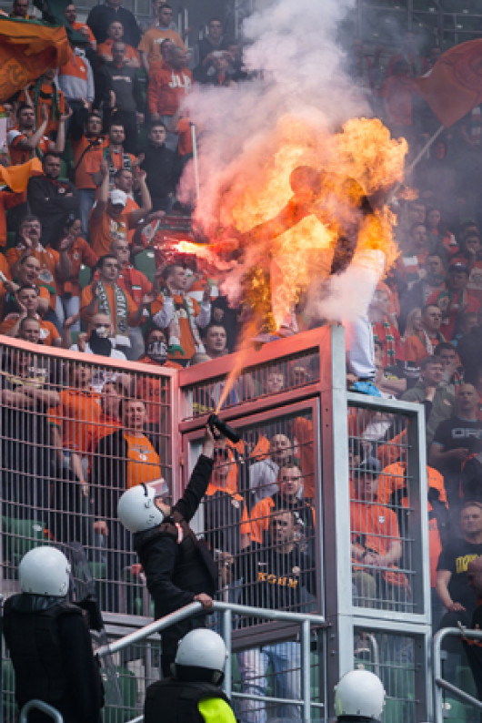 II miejsce w kat. WYDARZENIA, fot. Sebastian Borowski, „Fakt” Wrocław. Podczas derbów Śląsk Wrocław – KGHM Zagłębie Lubin na stadionie miejskim kibice odpalali race. Jeden z kibiców Lubina szczególnie się wyróżniał: wchodził na ogrodzenie, machał zapaloną racą w kierunku stewardów. Był zamaskowany. Gdy obok trybun pojawił się szpaler ochroniarzy, jeden miał w ręce coś na kształt gaśnicy, lecz jak się okazało, był to gaz pieprzowy. Gdy go użył, w zetknięciu z racą niespodziewanie powstał pożar i kibic na moment zapłonął jak pochodnia. Nie doznał obrażeń; przed poparzeniem twarzy uchroniła go kominiarka. 26 kwietnia 2014 